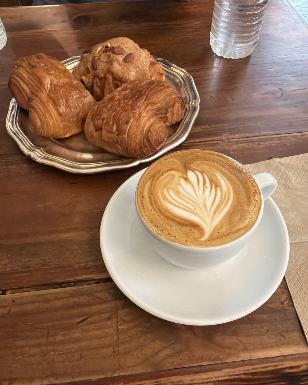 Latte with leaf latte art and a plate of pastries on a wooden cafe table in France
